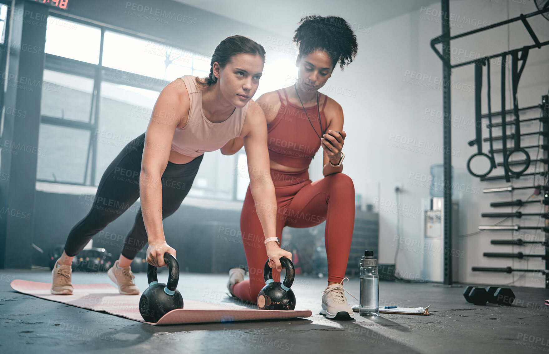 Buy stock photo Personal trainer, kettle bell and stopwatch with a black woman coaching a client in a gym for her workout. Health, exercise or training and a female athlete doing a plank with her coach taking time