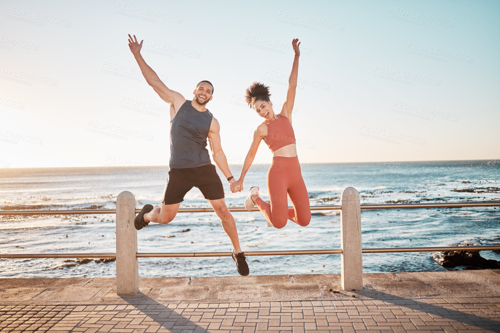 Buy stock photo Fitness, jump and portrait of a couple at beach for training fun, support and celebration of goal. Energy, happy and excited man and woman jumping while holding hands at the sea for cardio in Spain