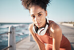 Portrait, fitness and black woman tired, ocean and runner with headphones, focus and determined for goal. African American lady, female exhausted and runner with podcast, rest and training for health