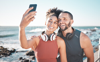 Buy stock photo Fitness, couple and phone for selfie at the beach with smile for running, exercise or workout together. Happy woman and man smiling in happiness looking at smartphone for photo after run by the ocean