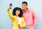Happy couple, tongue and phone selfie on isolated blue background for social media, city profile picture and travel vlog. Man, black woman and silly faces bonding for on mobile photography technology