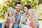 Family, bubbles and park fun outdoor feeling happiness, love and parent care with children. Happy mom, dad and girl kids in nature on grass relax on vacation on summer holiday together with a smile