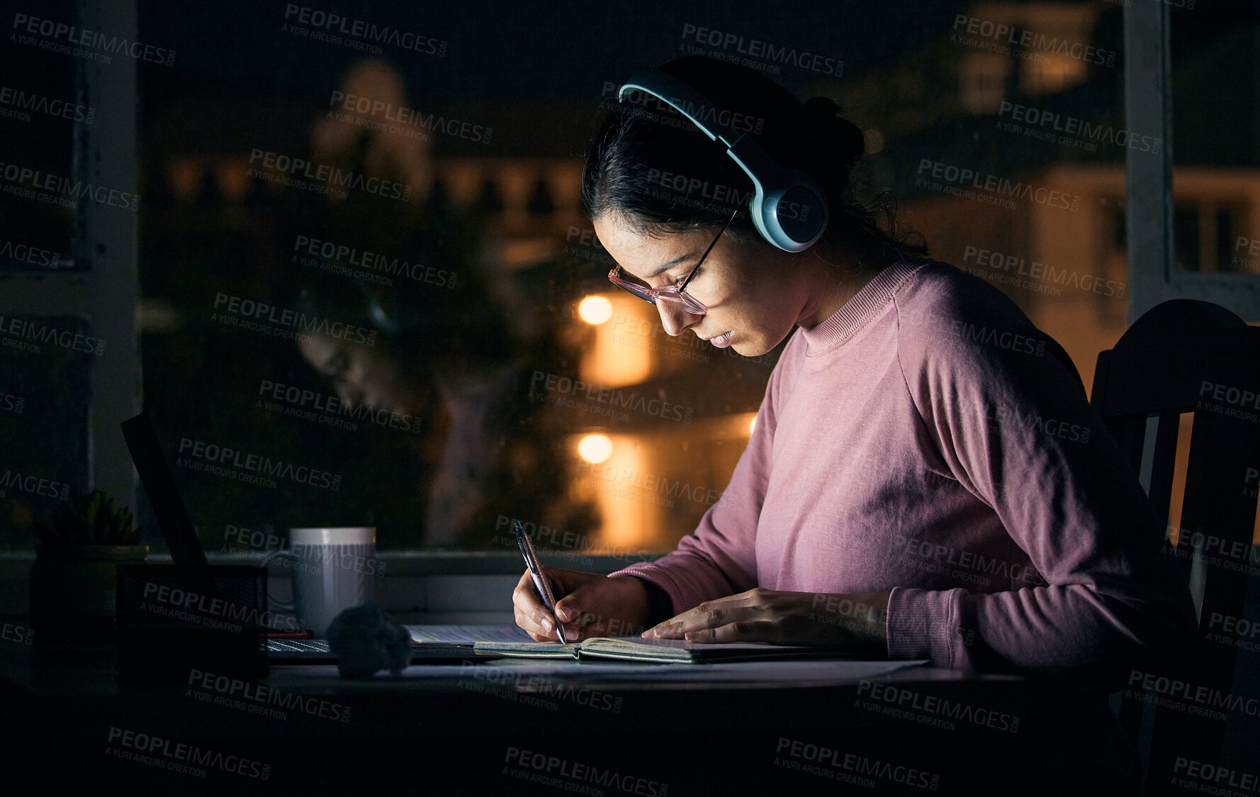 Buy stock photo Headphones, writing and student studying at night for a test, exam or college assignment. University, notes and woman doing research while listening to music, radio or podcast in the evening at desk.