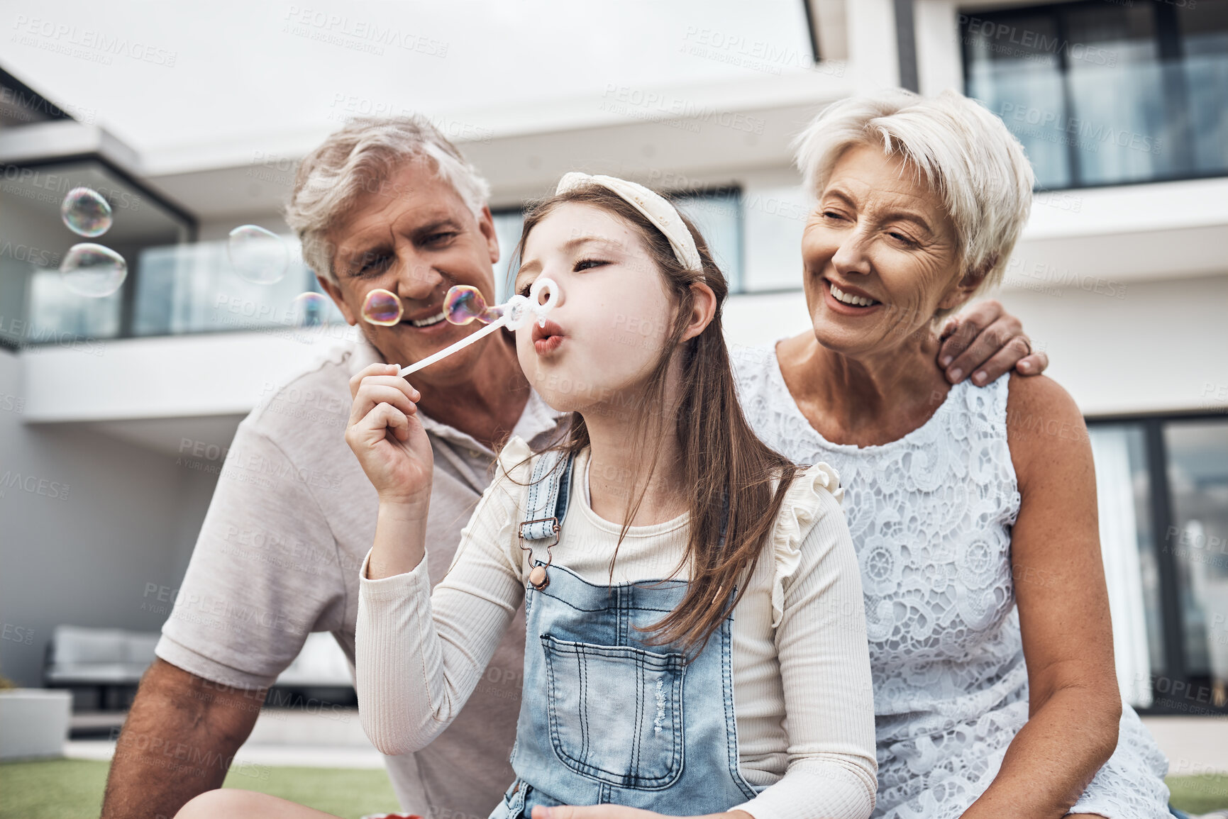 Buy stock photo Smile, family and girl with bubbles and grandparents enjoying weekend, holiday and quality time together. Love, home and happy girl, grandmother and grandfather bonding, relaxing and fun in garden