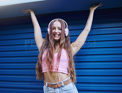 Buy stock photo Portrait, music or freedom with a woman on a blue background standing arms raised in celebration for fun. Party, fashion and headphones with an attractive young female streaming or listening to audio