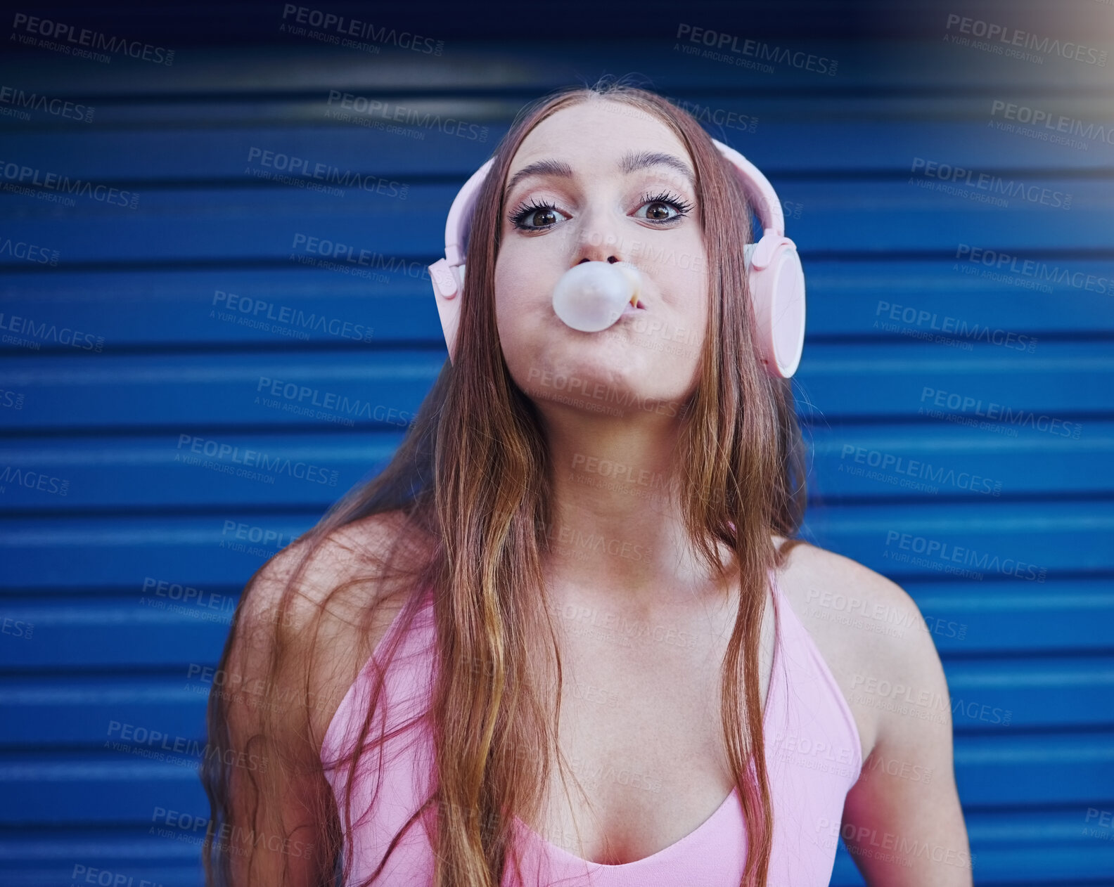 Buy stock photo Young woman, bubblegum and headphones, face isolated on blue background, listen to music with freedom and fashion. Blowing bubble, candy and crazy gen z youth in studio, fun with radio or audio tech