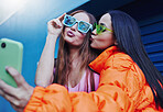 Selfie, fashion and friends with smartphone on blue background with style, cool sunglasses and urban clothes. Social media, freedom and women smile for photo on weekend, vacation and holiday in city