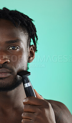 Buy stock photo Shaving face with razor, black man in studio and skincare for smooth facial hair on green background. Confident young model grooming, hygiene and cleaning beard with cosmetic morning routine
