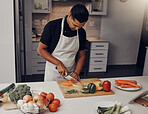 Cooking, food and vegetables with a man cutting ingredients in the kitchen on a wooden chopping board. Salad, health and diet with a male chef preparing a meal while standing alone in his home