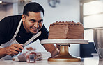 Baking, small business and happy man icing cake with chocolate frosting and piping bag in bakery with smile. Sweets, skill and baker decorating dessert for birthday event and chef working in kitchen.