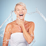 Skincare, grooming and portrait of an excited woman with a water splash isolated on a blue background in studio. Cleaning, hygiene and smile of a senior model with body and self care on a backdrop
