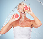 Woman, studio portrait and grapefruit with water splash, smile and happy for wellness by blue background. Senior model, organic citrus fruit and vitamin c for health, nutrition and self care process