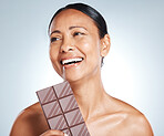 Chocolate, smile and senior woman thinking of health isolated on a blue background in studio. Food, happy and face of an elderly model with an idea for candy, sugar snack and sweets on a backdrop