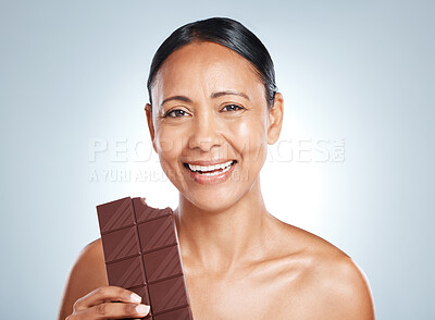 Buy stock photo Candy, health and portrait of a woman with chocolate isolated on a blue background in studio. Food, happy and face of an elderly model showing a treat, sugar snack and sweets with smile on a backdrop