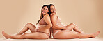 Pregnant woman friends, studio and underwear with smile, sitting and together for support by backdrop. Happy women, pregnancy and solidarity for wellness, care and holding healthy stomach by backdrop