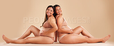 Buy stock photo Pregnant woman friends, studio and underwear with smile, sitting and together for support by backdrop. Happy women, pregnancy and solidarity for wellness, care and holding healthy stomach by backdrop