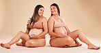 Women, bonding or sitting with pregnant stomach, tummy growth progress or baby healthcare wellness on studio background. Smile, happy or friends in pregnancy underwear for solidarity support or love
