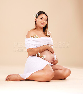 Buy stock photo Pregnancy, beauty and portrait of a woman in studio with chiffon material and flowers holding her stomach. Maternity, prenatal health and pregnant female model with floral posing by beige background.