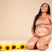 Pregnancy, mother and portrait of pregnant black woman with sunflower  plants happy isolated in brown studio background. Baby, motherhood and  future mom holding her tummy, stomach or abdomen for care