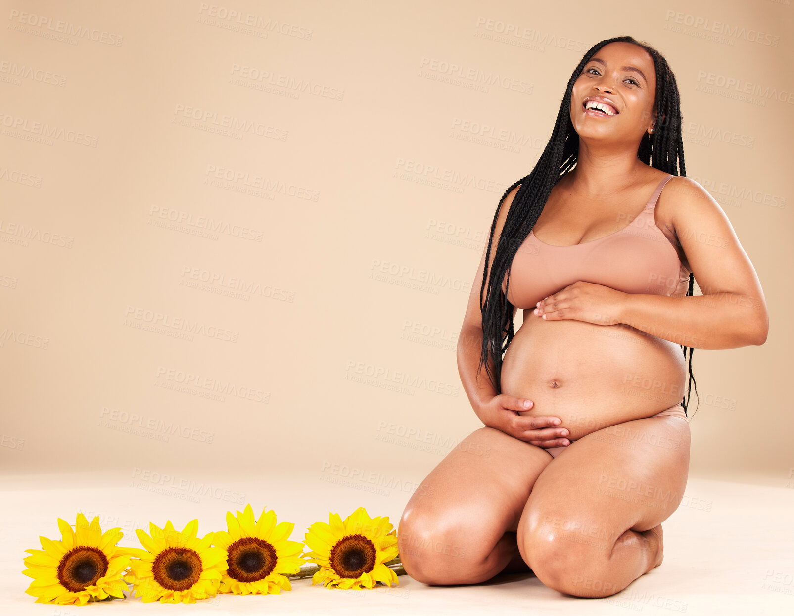 Buy stock photo Pregnancy, mother and portrait of pregnant black woman with sunflower plants happy isolated in brown studio background. Baby, motherhood and future mom holding her tummy, stomach or abdomen for care