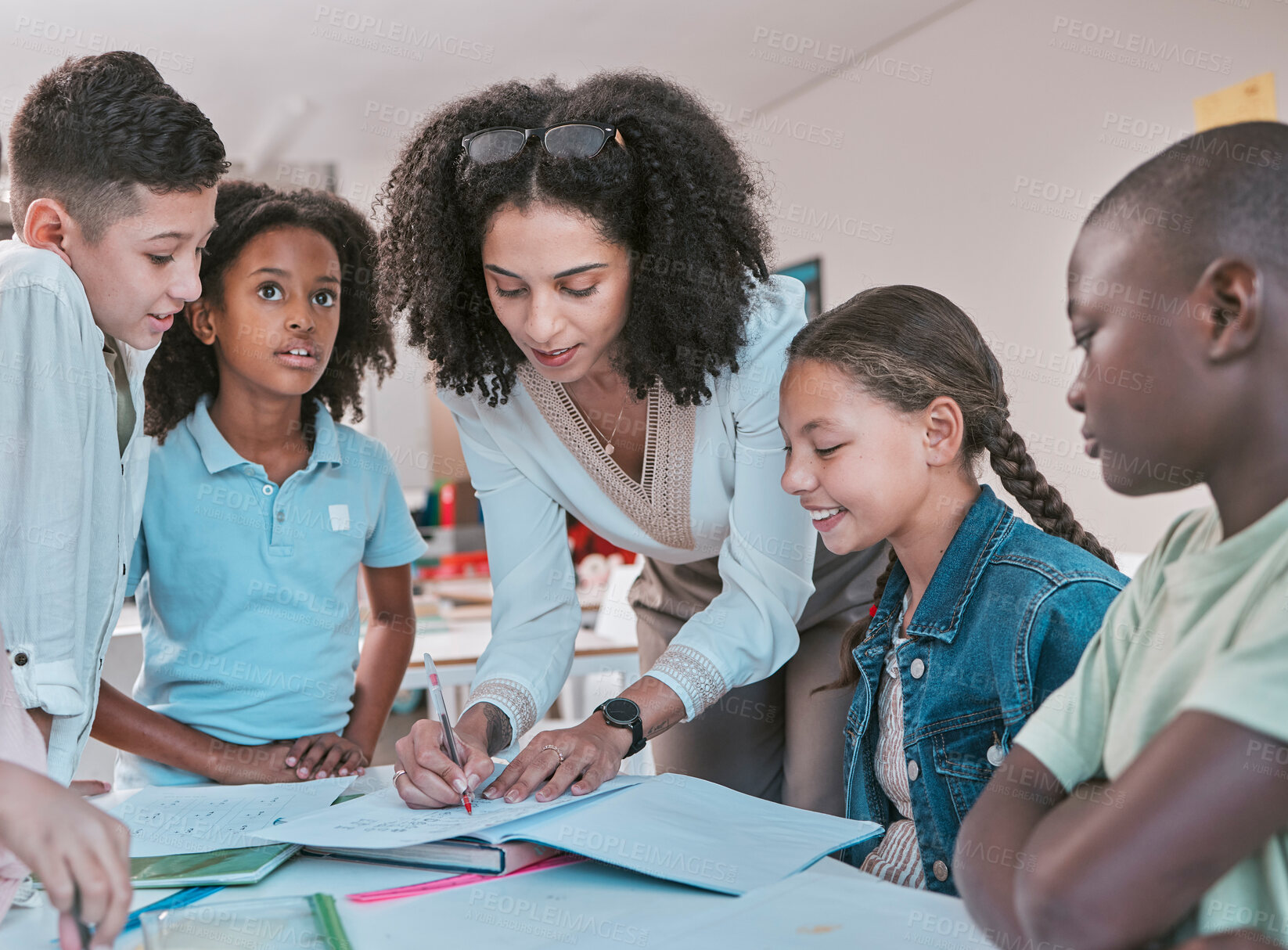 Buy stock photo Female teacher in classroom with children, helping girl student with schoolwork and writing in book. Diversity in education, educator reading kids notebook and group learning together for assessment