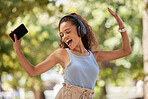 Phone, music and dance with a black woman listening to the radio in the park during summer while feeling free. Freedom, sing and dancing with an attractive young female streaing audio in a garden