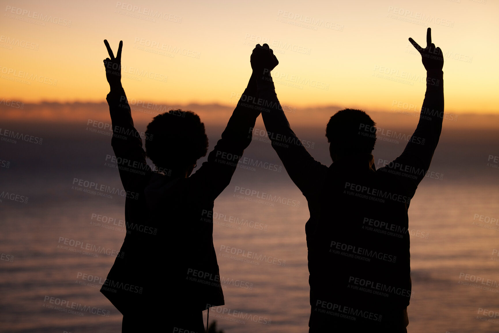 Buy stock photo Sunset, beach and silhouette of couple celebration, success or winning and holding hands in shadow, night or dark. Sky, ocean and winner people in rear with peace sign for sea, hiking or travel goals