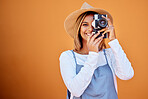 Photographer, portrait and woman shooting a picture or photo with a retro camera isolated in an orange background. Happy, studio and taking creative shots or fashion photographs as photography