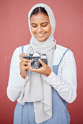 Buy stock photo Muslim, hijab and photographer shooting a picture or photo with a retro camera isolated in a studio red background. Islam, Dubai and woman in scarf happy taking creative shots for photography
