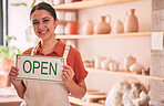 Woman, pottery art and small business with open sign for creative startup, welcome or entrepreneurship at retail store. Portrait of happy entrepreneur with smile holding opening board ready at shop