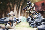 Paintball, gun or people play in a shooting game with fast action on a fun battlefield on holiday. Man on mission, fitness or player jumping with weapons gear for survival in an outdoor competition