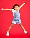 Excited, playful and portrait of a girl jumping while isolated on a red background in a studio. Youth, smile and child with freedom, energy and happiness while playing with a jump on a backdrop