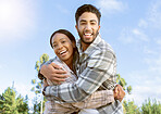 Portrait, couple of friends and hug while hiking in nature, forest and park. Diversity, man and woman embrace outdoors for journey, travel and adventure together on blue sky with love, smile or care 