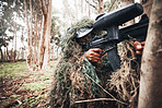 Paintball gun, forrest and man with aim by trees for outdoor war game, strategy or focus in natural camouflage. Shooter, sniper and helmet for safety with eyes on target for winning in military games