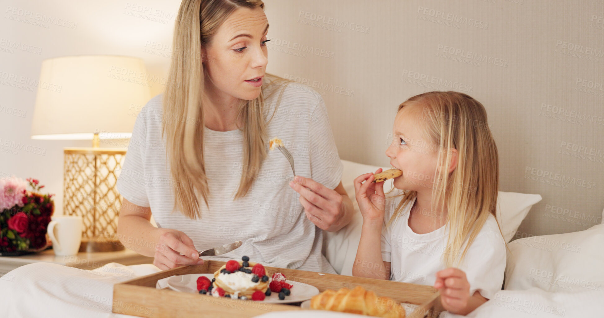 Buy stock photo Mother, child and breakfast in the bed together on mothers day, morning and talking in home and eating food or pancakes. Girl, mom and bite of healthy strawberry, croissant or bonding in bedroom