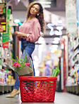 Grocery basket, store and floor with shopping, black woman or flowers on sale, discount or valentines promotion. Young female person, low angle and search shelf for product, groceries or food in shop