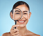 Magnifying glass, face portrait and skincare of woman in studio isolated on a blue background. Beauty search, makeup and cosmetics of female model with magnifier lens to check aesthetic wellness.