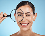 Face portrait, magnifying glass and skincare of woman in studio isolated on a blue background. Beauty search, makeup and cosmetics of female model with magnifier lens to check aesthetic wellness.