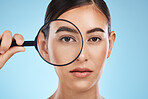 Woman, face with magnifying glass, eyes and beauty in portrait, eye care and vision isolated on blue background. Skincare cosmetics, skin and facial inspection, mockup space and dermatology in studio