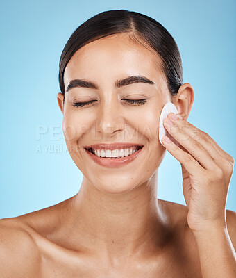 Buy stock photo Beauty, cotton pad and woman in a studio removing makeup, cosmetic or face glamour. Self care, skincare and happy female model with a healthy facial or skin routine isolated by a blue background.