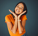 Woman, happy and hands on face portrait in studio for smile, beauty and motivation for happiness. Model person with orange t-shirt for fashion, positive mindset and mental health on a blue background