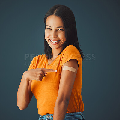 Buy stock photo Black woman, portrait and covid plaster in studio for vaccine, safety or wellness by blue background. Happy gen z girl, fashion and pointing for healthcare, medicine or lifestyle choice to stop virus