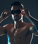 Fitness, sports and face of swimmer with goggles isolated in studio for wellness, exercise and training. Workout, swimming athlete and man focus on dark background with muscle, strong body and tattoo