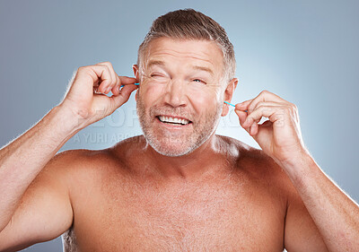 Buy stock photo Earbuds, health and man cleaning his ears in a studio for self care and funny hygiene. Beauty, wellness and healthy mature guy doing his morning grooming routine isolated by a gray background.