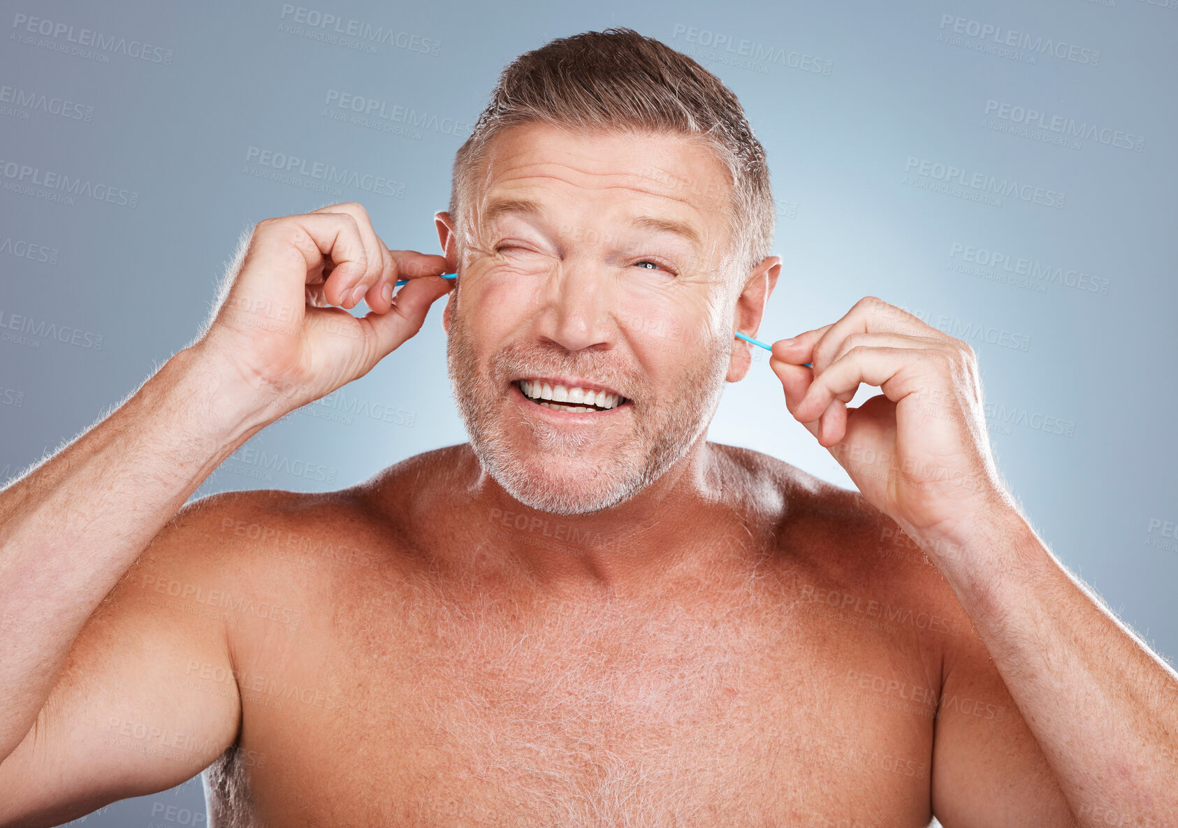 Buy stock photo Earbuds, health and man cleaning his ears in a studio for self care and funny hygiene. Beauty, wellness and healthy mature guy doing his morning grooming routine isolated by a gray background.