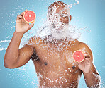 Black man, water splash and fruit for skincare nutrition, vitamin C or hydration against a blue studio background. Happy African American male smiling and holding grapefruit for health and wellness