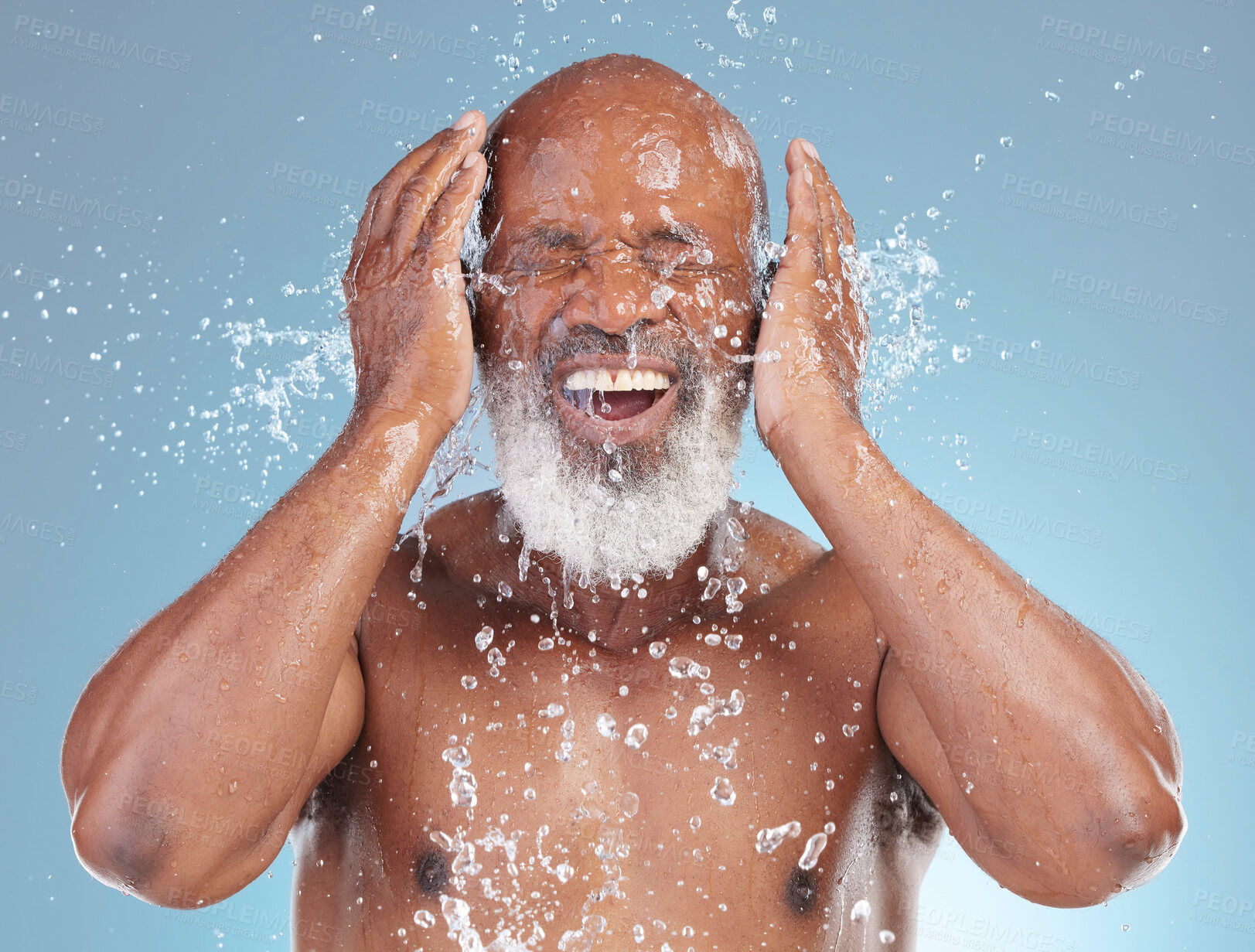 Buy stock photo Water splash, beauty and black man isolated on blue background for face cleaning, beauty and hands skincare. Happy senior model or person with facial wash or hygiene for dermatology in studio action