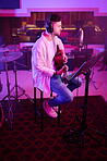 Artist, headphones or guitar in neon studio, recording production or performance on radio mic, label or band concert. Guitarist, musician or man playing on strings instrument in night light practice