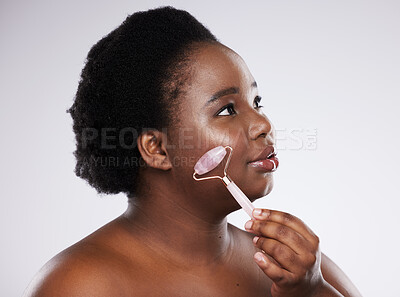 Buy stock photo Skincare, face and massage with a model black woman in studio on a gray background using a roller. Facial, luxury and beauty with a young plus size female indoor to promote an antiaging product