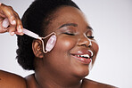 Black woman, studio and skincare, rose quartz roller for cosmetic beauty, smooth and healthy glow on face. Model, happy and massage skin for health, wellness and beauty by gray background with smile